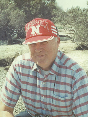 Jim, who grew up in Nebraska, sits outside wearing a University of Nebraska-Lincoln Huskers hat.